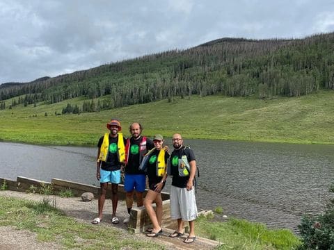 Five Mini Money crew members in matching shirts standing at the edge of a mountain lake.