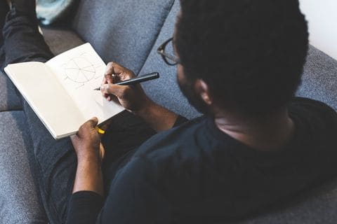 Hands sketching a circular plan diagram in a notebook, seen from above.